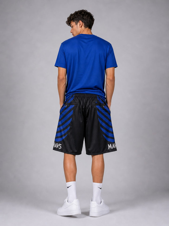 Hoopers Dallas Mavericks black and blue striped basketball shorts with 'MAVS' text. Model is wearing a blue t-shirt and white sneakers.