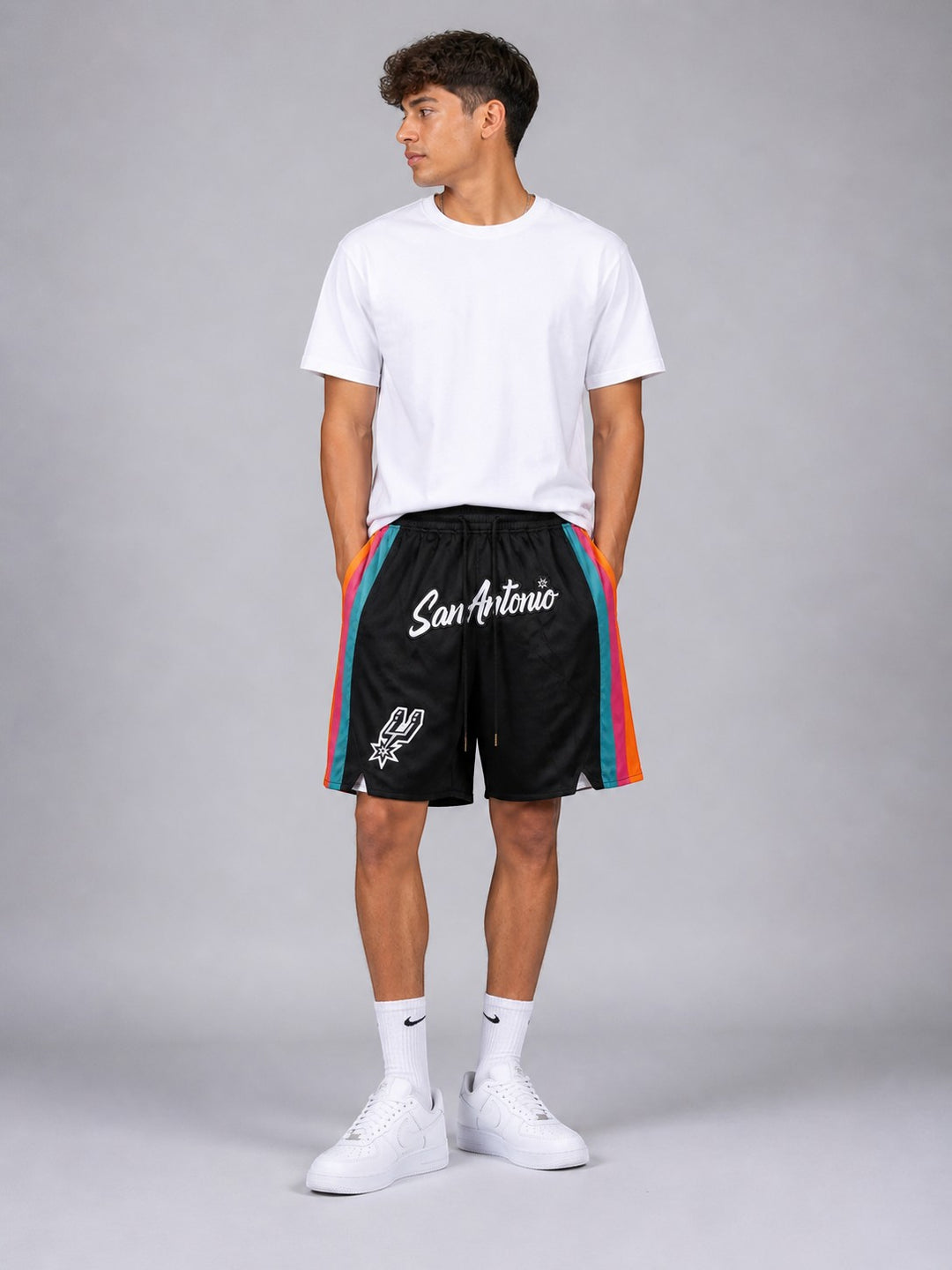 Hoopers San Antonio Spurs black NBA shorts with colorful side stripes and team logo. Model is wearing a white t-shirt and sneakers.