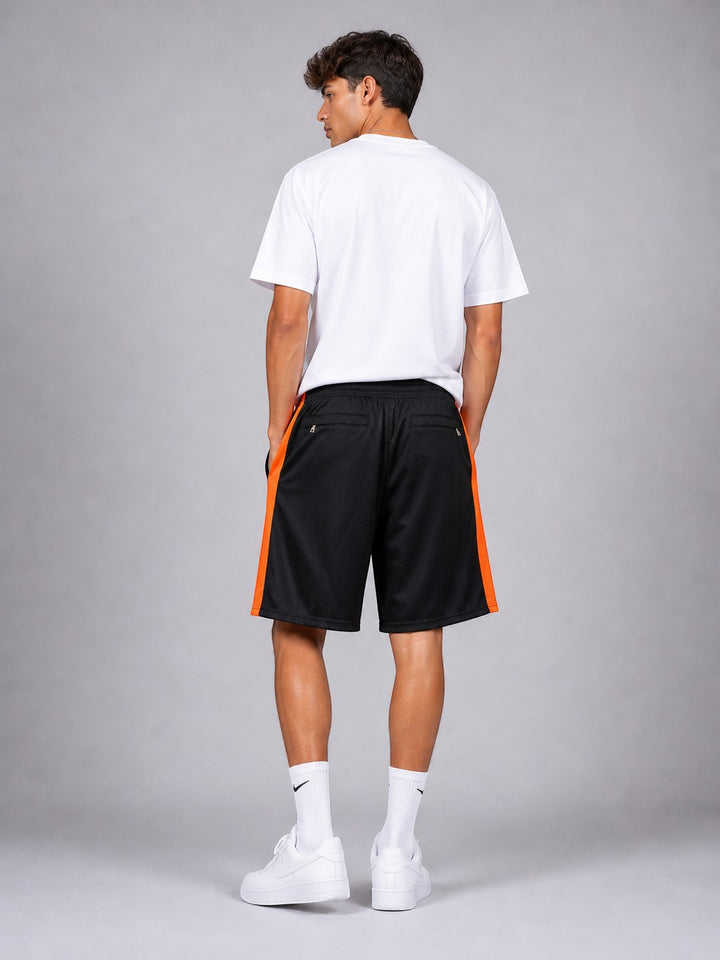 Hoopers black NBA shorts with orange side stripes, mesh fabric, wide leg, and pockets. Model is wearing a white t-shirt and white socks.